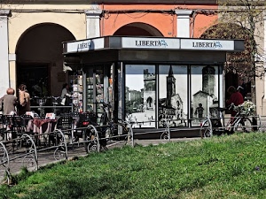 edicola, erba, verde, archi, portici, sedie, aiuola, giornali, persone, prato, tavolino, biciclette, recinzione, tavoli, tavolini, fotografie, ringhiera, metallo, libertà, inferriata